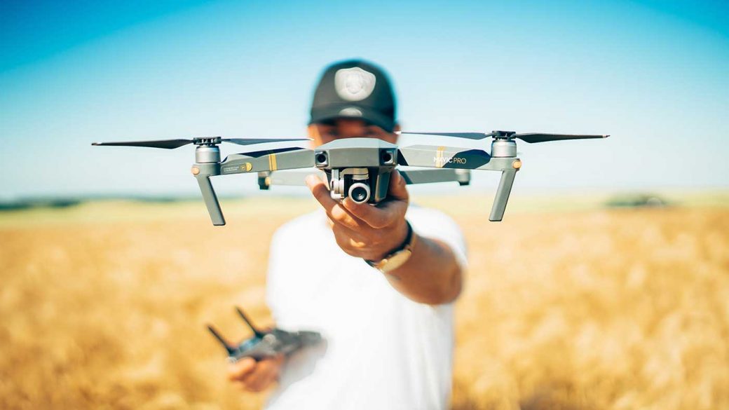 Drone pilot holding a drone and radio transmitter in a field