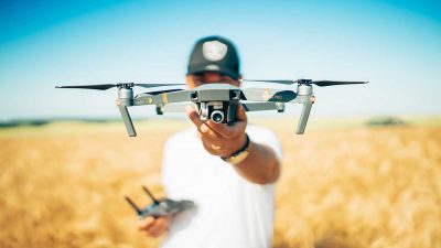 Drone pilot holding a drone and radio transmitter in a field