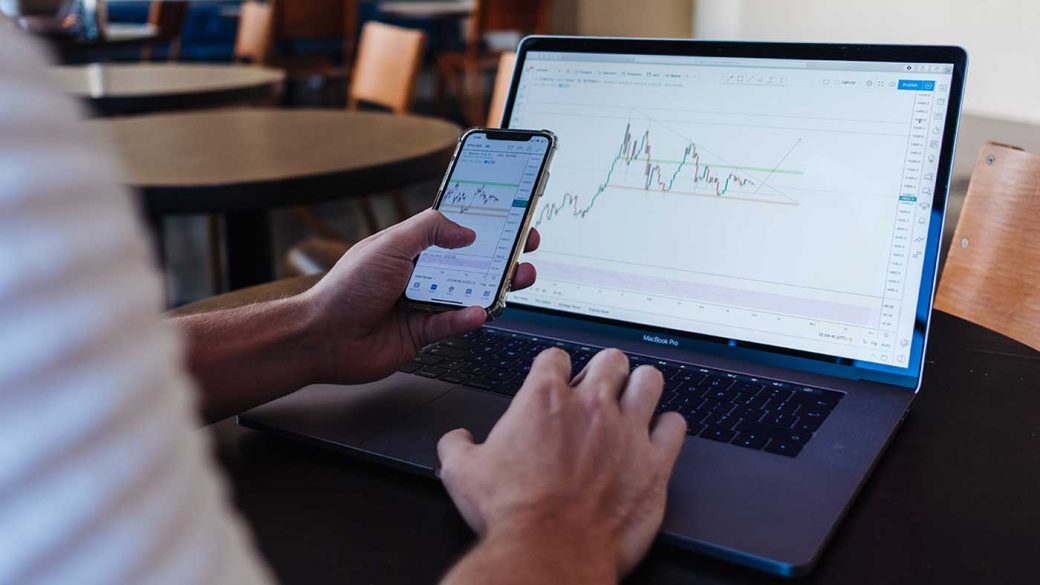 Financial investor using an electronic trading platform on their phone and laptop