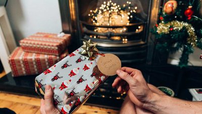 Man opening a Secret Santa Christmas gift by the fireplace