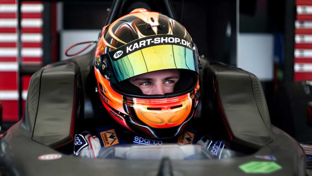 Racing driver wearing an orange helmet sitting in an open-wheel race car cockpit