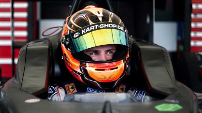 Racing driver wearing an orange helmet sitting in an open-wheel race car cockpit
