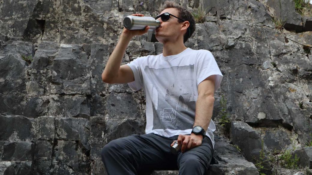 Drinking water from a stainless steel bottom while sat on a rock