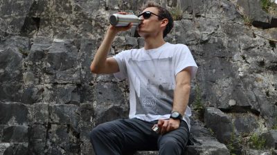 Drinking water from a stainless steel bottom while sat on a rock
