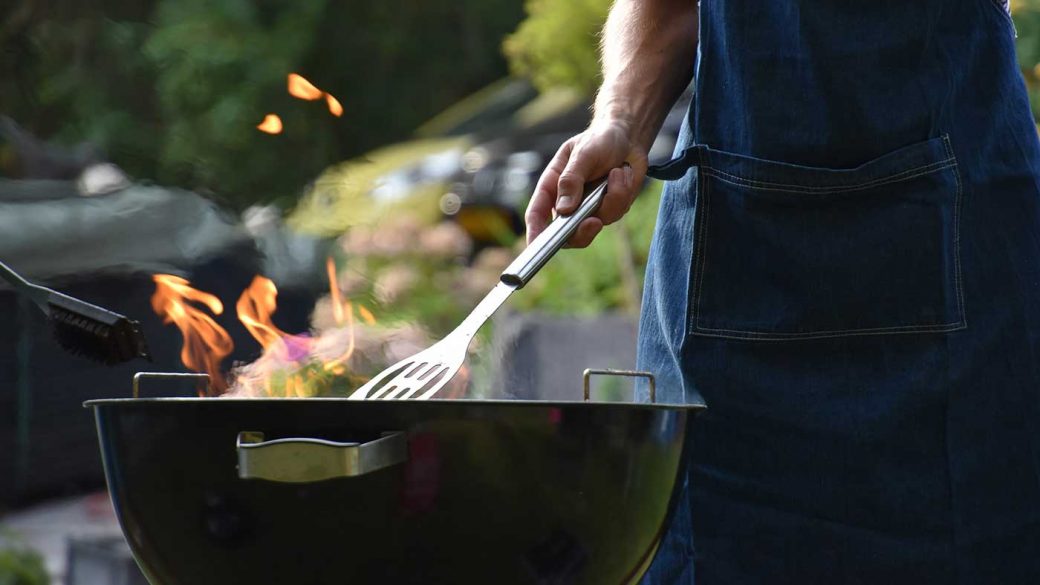 Man wearing a blue apron and using tips for a perfect barbecue