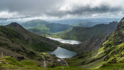 Looking down across two lakes surrounded by mountains under a cloudy sky in Snowdonia National Park