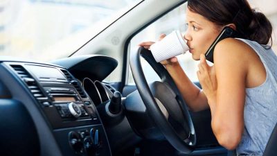 Woman being distracted while driving a car by drinking coffee and chatting on the phone
