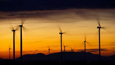 Silhouetted wind turbines against an orange sunset sky with mountains in the background, showcasing the advantages of measurement and control solutions in renewable energy applications.